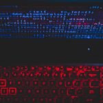 Dark-themed laptop setup with a red glowing keyboard and code on screen, ideal for tech enthusiasts.